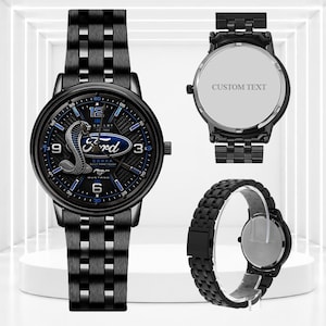 Pode incluir: Um relógio de pulso de aço inoxidável preto com o logótipo Ford Mustang Cobra no mostrador, detalhes em azul e uma bracelete de elos. O relógio é mostrado de frente, de costas e de lado, com o texto CUSTOM TEXT na parte traseira.
