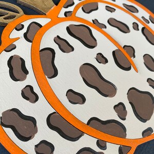 May include: A white pumpkin with brown spots and an orange outline. The pumpkin is painted with a leopard print pattern.