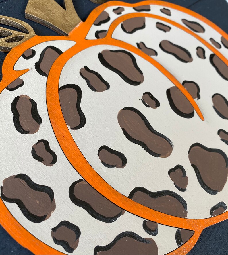 May include: A white pumpkin with brown spots and an orange outline. The pumpkin is painted with a leopard print pattern.
