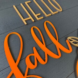 May include: A wooden sign with the words "Hello Fall" in gold letters and "Fall" in orange letters.