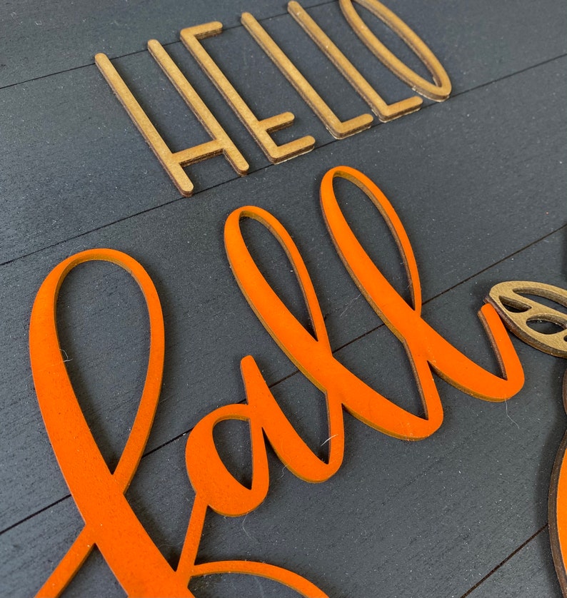 May include: A wooden sign with the words "Hello Fall" in gold letters and "Fall" in orange letters.