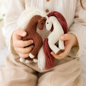 May include: Two handmade crochet horses, one dark brown with a cream mane and tail, and one cream with a dark red mane and tail. The horses are positioned facing each other with their heads touching, creating a heart-shaped space between them.