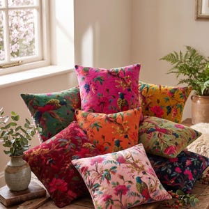 Peut inclure: Une collection de coussins carrés en velours dans des tons variés comme le rose vif, l'orange, le rouge profond, le jaune et le rose pâle. Chaque coussin présente un imprimé détaillé d'oiseaux exotiques sur des branches fleuries.
