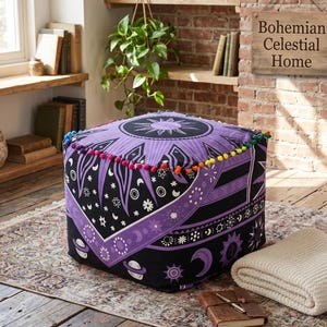 Può includere: Pouf quadrato nero e viola con design celeste, con motivi di sole, luna e stelle. Il pouf ha un bordo con pompon colorati ed è posto su un tappeto fantasia. Il cartello sullo sfondo recita "Bohemian Celestial Home".