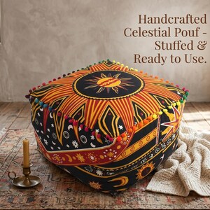 May include: Handcrafted celestial pouf with a vibrant sun and moon design. The square pouf features a black background with orange and yellow sunburst patterns. It is trimmed with colorful pom-poms and includes the text "Handcrafted Celestial Pouf - Stuffed & Ready to Use."