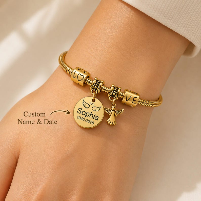 May include: Gold-tone charm bracelet with a snake chain. The bracelet has charms spelling "LOVE", a heart, and an angel pendant. A round charm is engraved with "Sophia" and dates. The text "Custom Name & Date" is also visible.