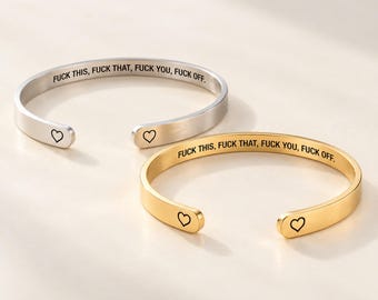 May include: Two open cuff bracelets, one in silver-tone and one in gold-tone metal. Each bracelet features the engraved text FUCK THIS, FUCK THAT, FUCK YOU, FUCK OFF along the inner band and a small black heart outline at each rounded end.