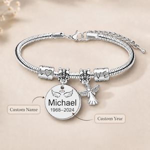 May include: A silver-toned snake chain bracelet featuring two cylindrical beads engraved with the word LOVE and a heart symbol, a dangling angel charm, and a round pendant engraved with the name Michael and the years 1968-2024 with angel wings.