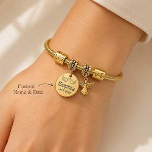May include: Gold-coloured charm bracelet with a snake chain design. The bracelet features charms with the words "LOVE", a heart, and an angel pendant. A round charm is engraved with the name "Sophia" and dates "1945-2028". The text "Custom Name & Date" is also visible.