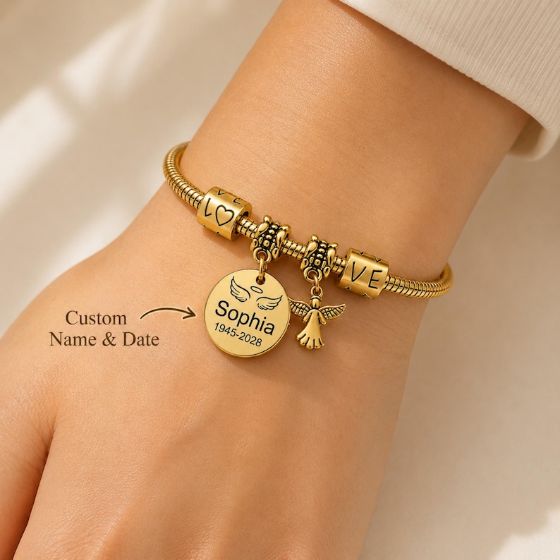 May include: Gold-coloured charm bracelet with a snake chain design. The bracelet features charms with the words "LOVE", a heart, and an angel pendant. A round charm is engraved with the name "Sophia" and dates "1945-2028". The text "Custom Name & Date" is also visible.