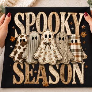 May include: A black fabric item featuring the text SPOOKY SEASON in a distressed beige font. Between the words are five ghost illustrations with different patterns including cow print, stripes, floral, cable knit, and plaid, with small stars.