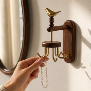 May include: A wall-mounted jewelry organizer featuring a dark brown wooden base and a rotating circular wooden platform. The structure is topped with a polished gold-toned bird figurine and includes multiple curved gold-toned metal hooks.