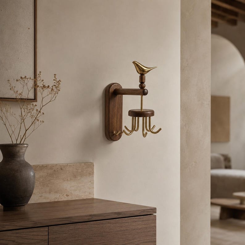 May include: A wall-mounted jewelry organizer featuring a dark brown wooden base and a horizontal arm. A polished gold-tone metal bird sits atop the arm, connected to a rotating circular wooden platform with six curved gold-tone metal hooks.