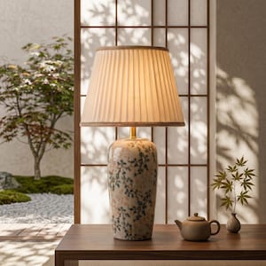 May include: A decorative table lamp with a pleated lampshade and a floral patterned base. The lamp sits on a wooden table, with a small teapot and vase nearby. The background features a Japanese-style garden.
