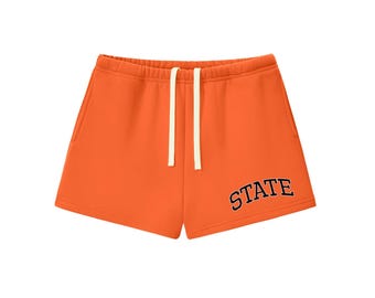 May include: Bright orange athletic shorts featuring an elastic waistband with two cream-colored drawstrings. The word STATE is printed in a dark navy blue collegiate-style font on the lower right leg of the garment.
