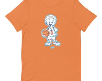 May include: An orange short-sleeve t-shirt featuring a cartoon basketball player graphic. The character wears a white headband with the text HUSTLE, a white jersey with OKC 9, and holds a basketball. The design includes blue outlines.
