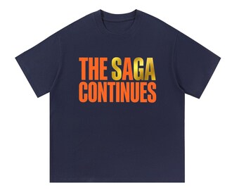 May include: A navy blue short-sleeve t-shirt featuring the text THE SAGA CONTINUES printed in a bold, gradient font that transitions from orange to a metallic gold hue across the center of the chest area on the garment.