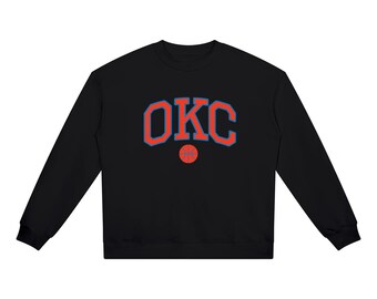 May include: A black long-sleeve sweatshirt featuring the text OKC in large, arched orange letters with a blue outline. Below the text is a small, circular orange basketball graphic with blue lines. The garment has a crew neckline and ribbed cuffs.