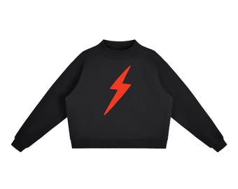 May include: A black long-sleeve sweatshirt featuring a mock neck collar and a vibrant red lightning bolt graphic centered on the chest. The garment has ribbed cuffs at the wrists and a ribbed hemline, providing a clean and structured silhouette.