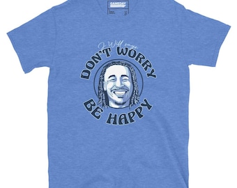 May include: A heather blue short-sleeve t-shirt featuring a graphic of a smiling person with dreadlocks inside a circle. The text "J Will says" appears above the circle, and the words "DON'T WORRY BE HAPPY" are printed in dark blue.