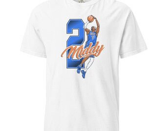 May include: A white short-sleeve t-shirt featuring a graphic of a basketball player in a blue jersey jumping to shoot a basketball. Behind the player is a large blue number 2 and the word Middy in orange script text across the center.