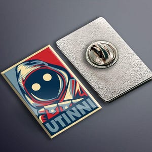 May include: A red, white, and blue enamel pin featuring a stylized illustration of a character with a large head and two eyes. The text "UTINNI" is printed in gold below the character.