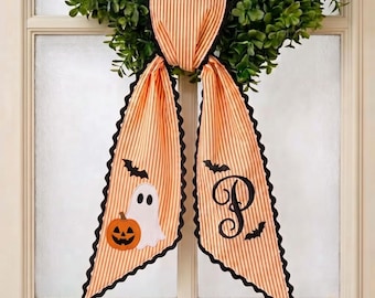 May include: A decorative fabric bow with orange and white vertical stripes and black scalloped edges. One tail features a white ghost and an orange jack-o'-lantern, while the other tail displays a black letter P and small black bat silhouettes.