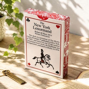 May include: A white rectangular deck of cards box titled The New York Lenormand by Robert M Place 2014. The box features red card suit symbols, a black illustration of a person riding a horse, and descriptive text about the deck's history.