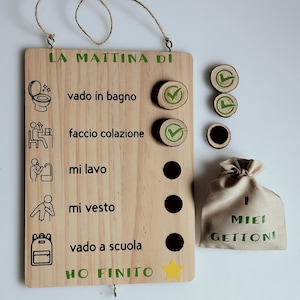 Può includere: Lavagna in legno per la routine mattutina con testo e illustrazioni verdi. Include gettoni di legno verificabili, un sacchetto con testo e una stella. La lavagna elenca le attività quotidiane in italiano.