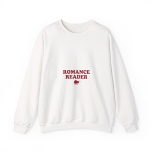 May include: White sweatshirt with the text "ROMANCE READER" in maroon letters and a small heart graphic. The long-sleeved top is made of a soft material and has a crew neck.