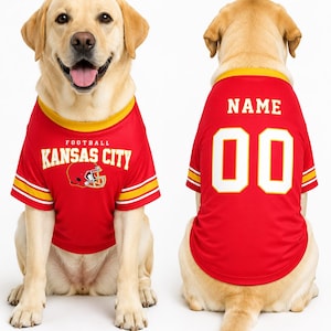 May include: Two dogs wearing red football jerseys. The front-facing dog's jersey reads "FOOTBALL KANSAS CITY" with a helmet graphic. The back-facing dog's jersey has "NAME" above the number "00". Both jerseys have yellow and white accents.