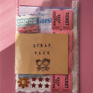 May include: A clear plastic bag containing a scrap pack of paper ephemera, including pink admission tickets, a guest check, patterned washi tape, a gold glitter flower, red star stickers, and a brown paper label printed with SCRAP PACK and a cartoon.