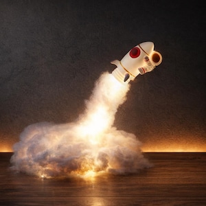 May include: A white and red toy rocket ship blasting off, with a trail of bright light and smoke. The rocket has red circular windows and is set against a dark background. The base of the rocket is surrounded by a cloud of white smoke.