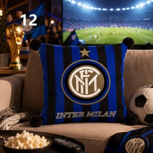 K&ouml;nnte beinhalten: Ein quadratisches Zierkissen mit vertikalen schwarzen und blauen Streifen, einem goldenen Stern und dem kreisf&ouml;rmigen Inter-Mailand-Logo mit dem Text INTER MILAN. Das Kissen hat an allen vier Ecken schwarze Bommeln und besteht aus Stoff.