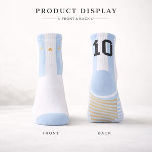 Puede incluir: Par de calcetines blancos y celeste con detalles de estrellas doradas y el n&uacute;mero 10 en la parte trasera. Los calcetines tienen un dise&ntilde;o a rayas y est&aacute;n etiquetados "FRONT" y "BACK". El texto "PRODUCT DISPLAY // FRONT & BACK //" est&aacute; en la parte superior.