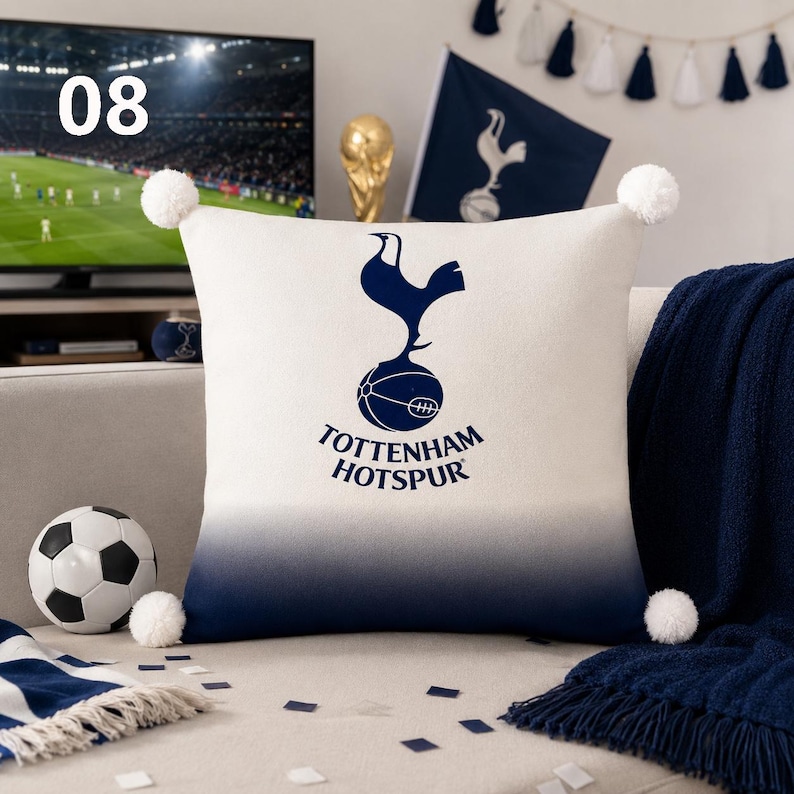 K&ouml;nnte beinhalten: Ein quadratisches Zierkissen mit dem dunkelblauen Tottenham Hotspur Logo und Schriftzug auf wei&szlig;em Grund, der nach unten hin in einen dunkelblauen Farbverlauf &uuml;bergeht. Das Kissen hat an jeder Ecke einen wei&szlig;en Bommel und eine glatte Oberfl&auml;che.