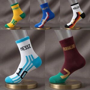 Peut inclure: Cinq paires de chaussettes de sport expos&eacute;es. Chaque chaussette pr&eacute;sente une combinaison de couleurs diff&eacute;rente et le nom d'un joueur de football. Les chaussettes sont jaunes, bleues, blanches, bordeaux et blanches. Chaque chaussette a un design diff&eacute;rent.