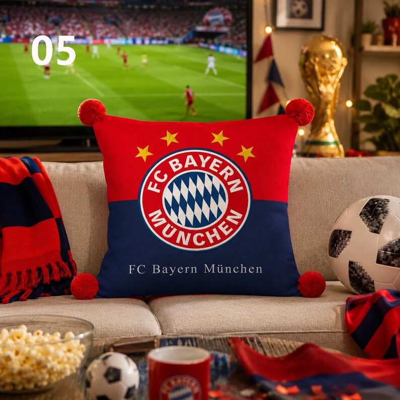 K&ouml;nnte beinhalten: Ein quadratisches Zierkissen mit dem FC Bayern M&uuml;nchen Logo in Rot und Marineblau. Das Design zeigt vier gelbe Sterne &uuml;ber dem runden Wappen und den Schriftzug FC Bayern M&uuml;nchen in Wei&szlig; am unteren Rand, erg&auml;nzt durch rote Bommeln an den Ecken.