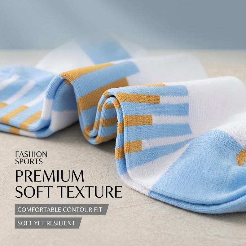 Puede incluir: Primer plano de calcetines blancos con rayas horizontales azules y doradas. Los calcetines est&aacute;n doblados, mostrando el patr&oacute;n y la textura. El texto en la imagen dice "FASHION SPORTS", "PREMIUM SOFT TEXTURE", "COMFORTABLE CONTOUR FIT" y "SOFT YET RESILIENT".