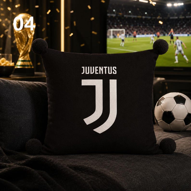 K&ouml;nnte beinhalten: Ein quadratisches schwarzes Dekokissen mit dem wei&szlig;en Logo des Fu&szlig;ballvereins Juventus und dem dar&uuml;ber gedruckten Wort JUVENTUS. Das Kissen ist an jeder seiner vier Ecken mit einem schwarzen Pompon versehen, der einen dekorativen Akzent setzt.