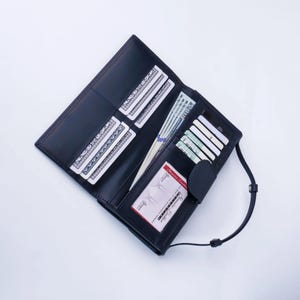 May include: Open black leather wallet with multiple card slots, holding cash and credit cards. The wallet has a strap and a snap closure. The wallet is open, displaying its contents against a white background.