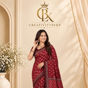 Peut inclure: Un sari rouge bordeaux profond orné d'un motif géométrique répétitif à petite échelle sur tout le tissu. Le vêtement présente une large bordure sombre aux détails complexes et un pan avec des panneaux horizontaux. L'ourlet est fini par des pompons.