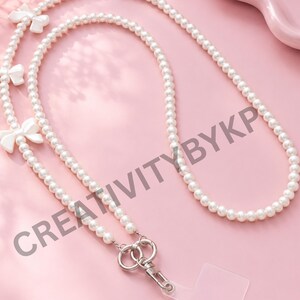 May include: A long lanyard made of white faux pearls featuring three small white bows attached to the strand. The lanyard includes a silver-toned metal clasp and a clear plastic tab connector. The text CREATIVITYBYKP is visible on the image.
