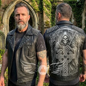May include: A black leather waistcoat featuring silver metal studs on the shoulders and collar. The back displays a detailed graphic of a hooded skeleton figure holding a large Celtic cross. The front includes a chest pocket and a snap-button pocket.