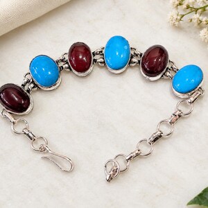 Könnte beinhalten: Ein silberfarbenes Gliederarmband mit abwechselnd ovalen Cabochon-Steinen in leuchtendem Türkis und tiefem Kastanienbraun. Das Armband verfügt über einen einfachen Hakenverschluss und kreisförmige Metallglieder, die die sieben polierten Steine verbinden.
