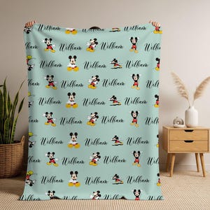 Puede incluir: Una manta azul claro con un patr&oacute;n repetido de Mickey Mouse y el nombre "William" en cursiva. La manta se muestra, destacando el dise&ntilde;o y la textura, ideal para una habitaci&oacute;n infantil.