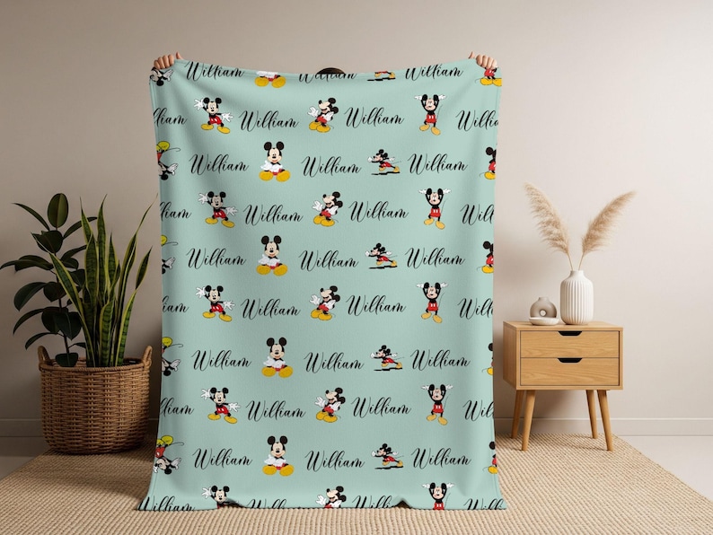 Puede incluir: Una manta azul claro con un patr&oacute;n repetido de Mickey Mouse y el nombre "William" en cursiva. La manta se muestra, destacando el dise&ntilde;o y la textura, ideal para una habitaci&oacute;n infantil.