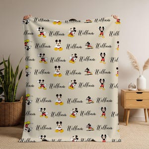 Puede incluir: Manta beige con un patr&oacute;n repetido de Mickey Mouse en varias poses y el nombre "William" en cursiva. La manta est&aacute; hecha de un material suave, ideal para ni&ntilde;os.