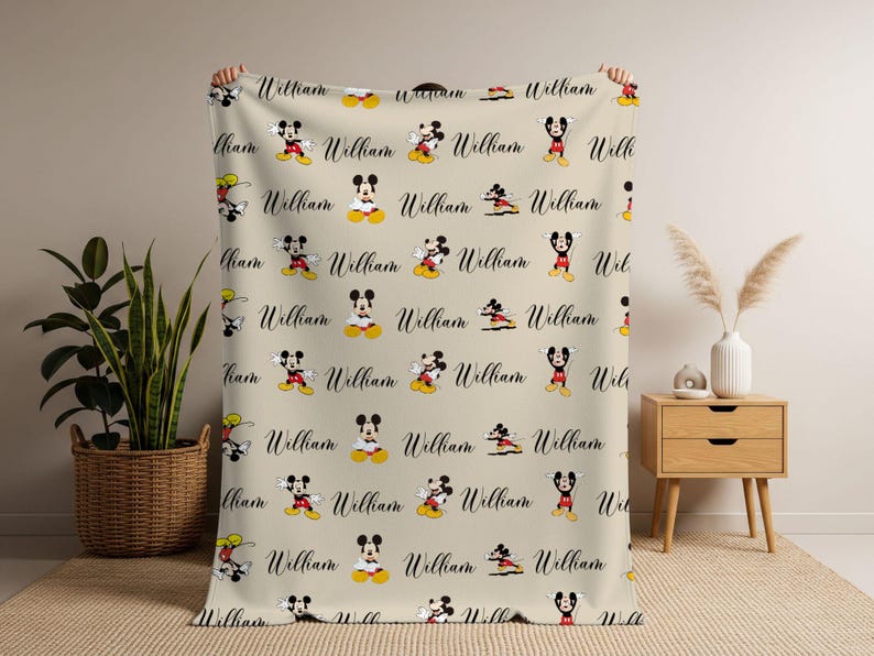 Puede incluir: Manta beige con un patr&oacute;n repetido de Mickey Mouse en varias poses y el nombre "William" en cursiva. La manta est&aacute; hecha de un material suave, ideal para ni&ntilde;os.
