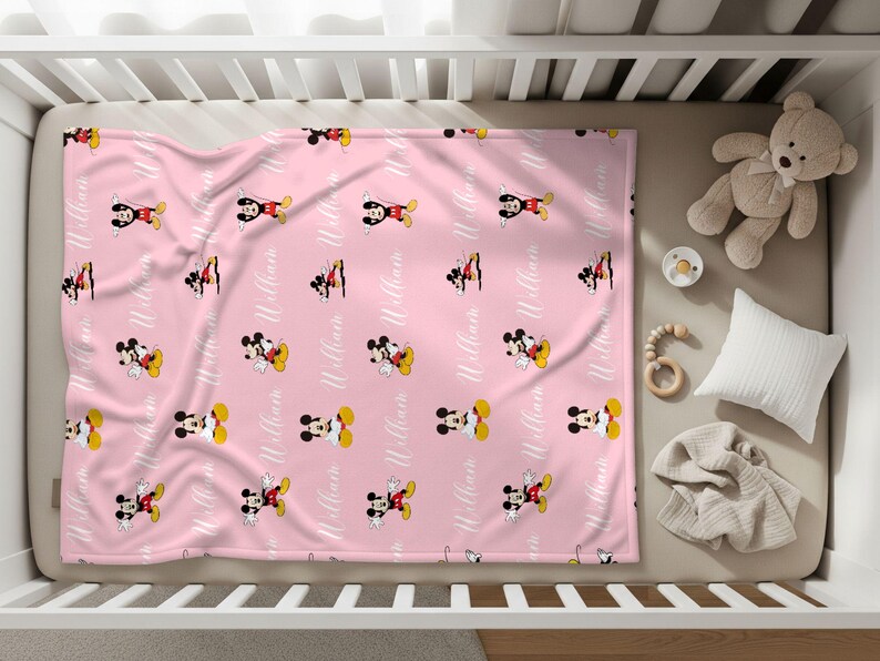 Puede incluir: Manta rosa para beb&eacute; con un patr&oacute;n repetido de Mickey Mouse en rojo, amarillo, negro y blanco. El nombre "William" est&aacute; impreso en escritura blanca. La manta est&aacute; en una cuna con un osito de peluche, un chupete y una almohada.